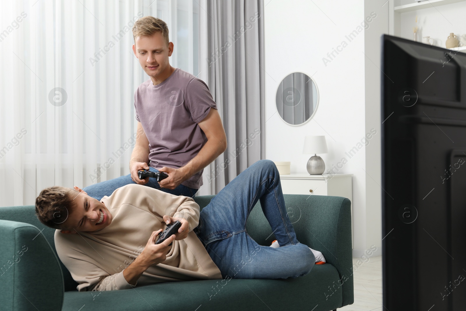 Photo of Young brothers playing video game on sofa at home