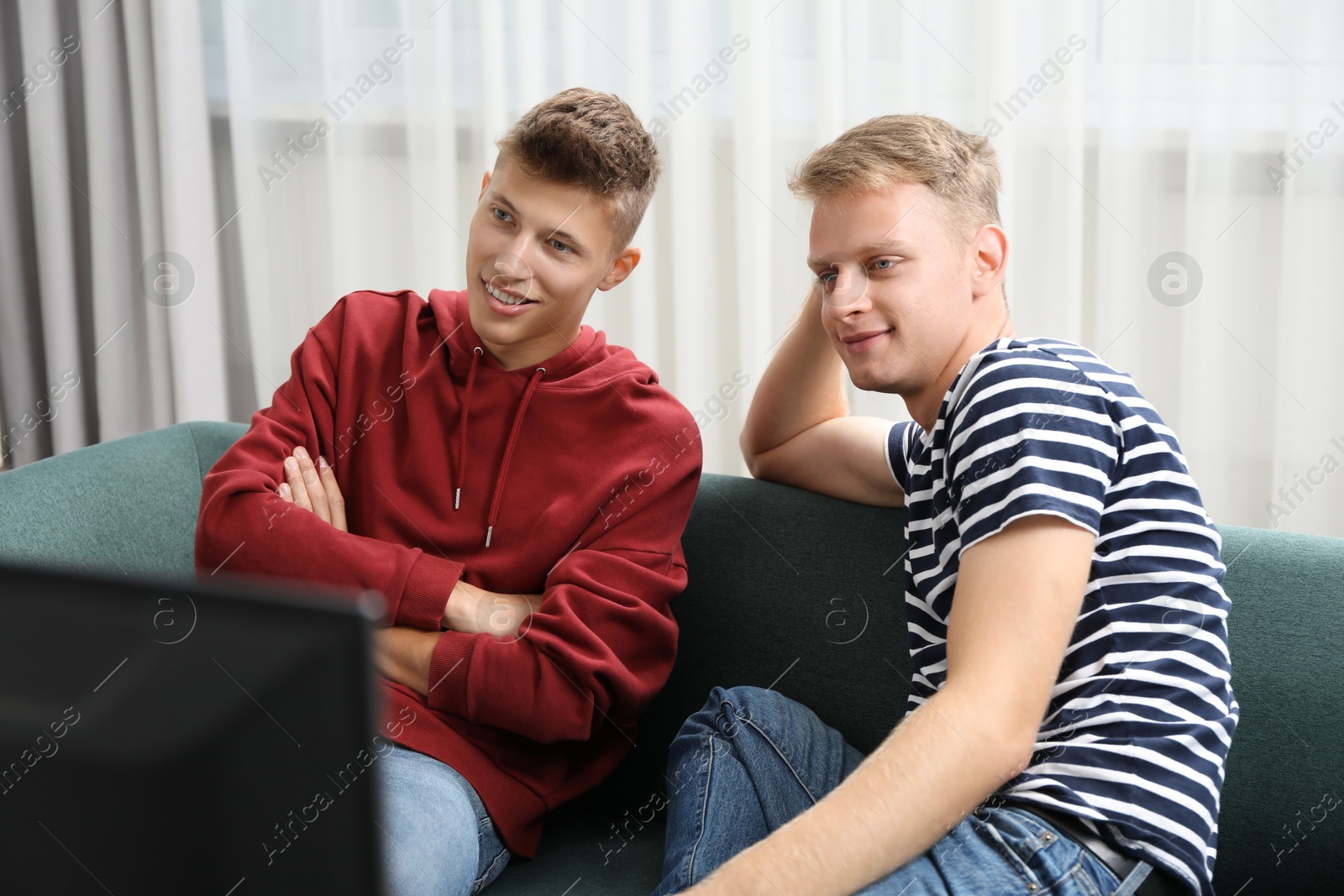 Photo of Young brothers watching tv on sofa at home