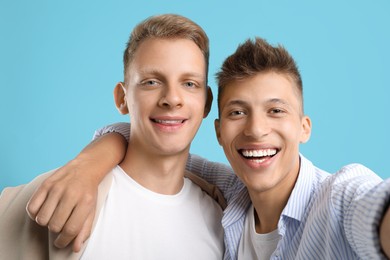 Happy brothers taking selfie on light blue background