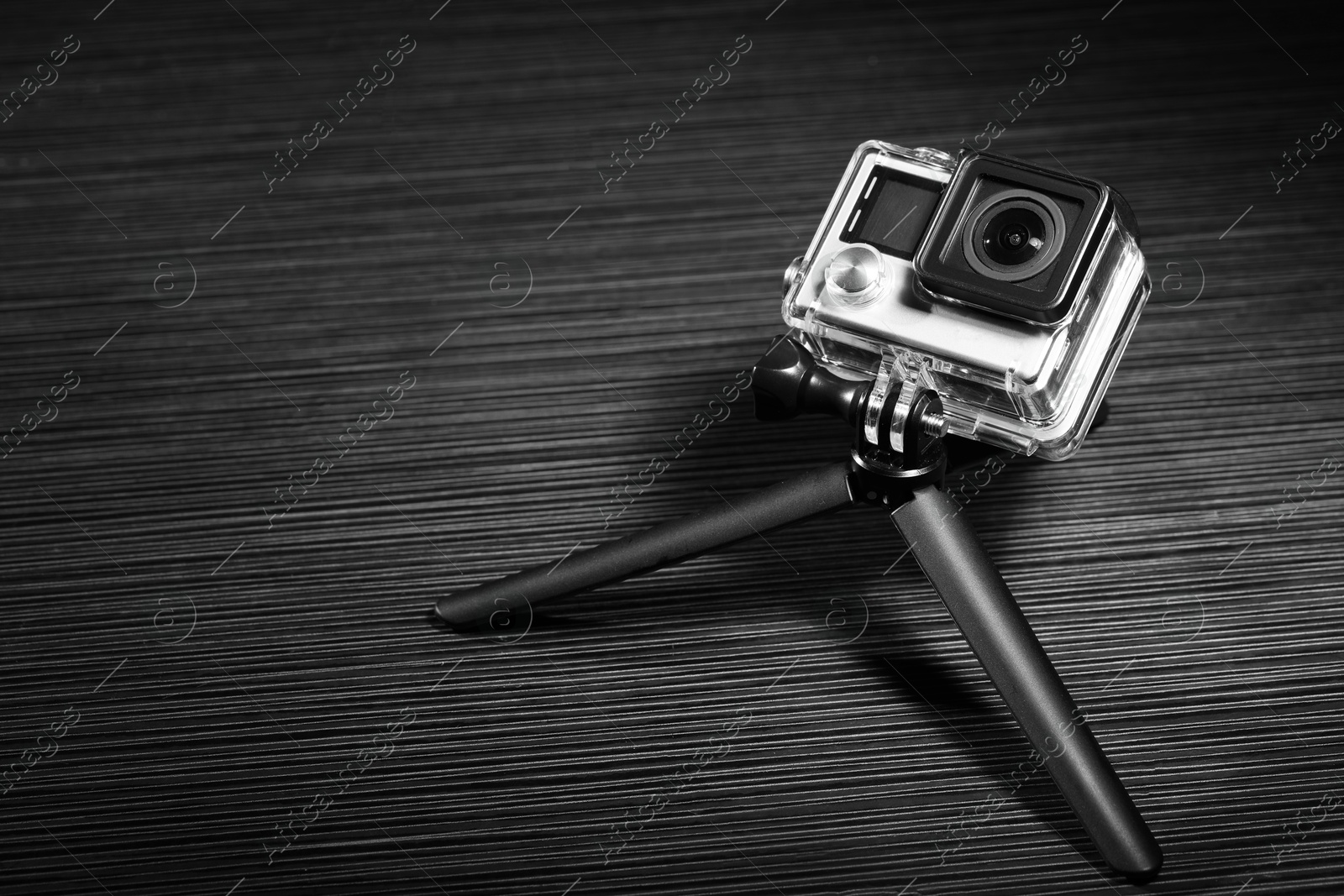 Photo of Modern action camera and tripod on grey wooden surface