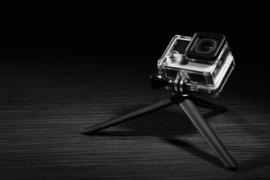 Photo of Modern action camera and tripod on grey wooden surface. Space for text