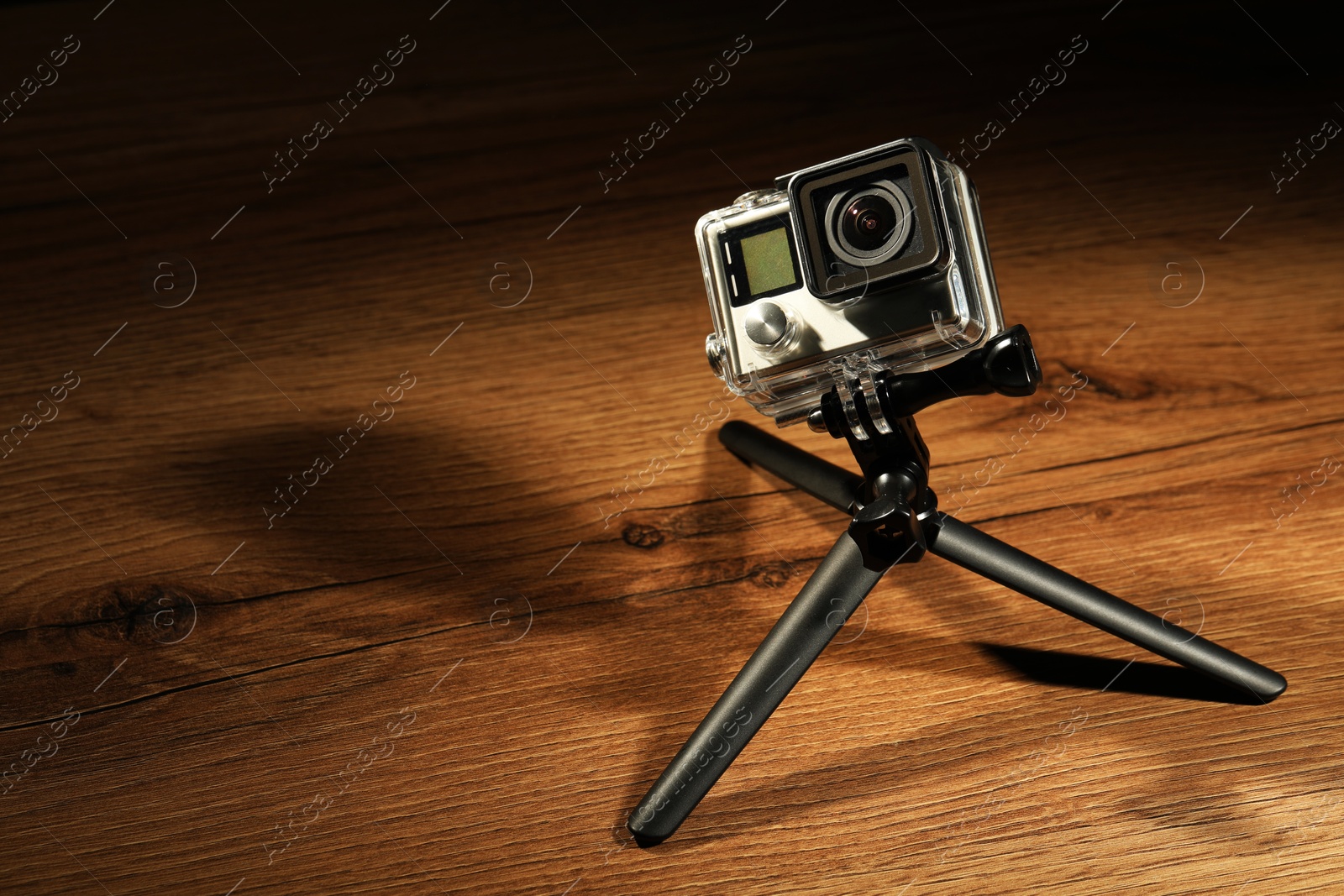 Photo of Modern action camera and tripod on wooden surface. Space for text