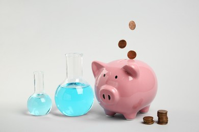 Photo of Water save concept. Piggy bank, coins and laboratory glassware with liquid on light grey background