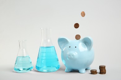 Water save concept. Piggy bank, coins and laboratory glassware with liquid on light grey background