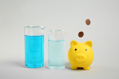 Photo of Water save concept. Piggy bank, coins and laboratory glassware with liquid on light grey background