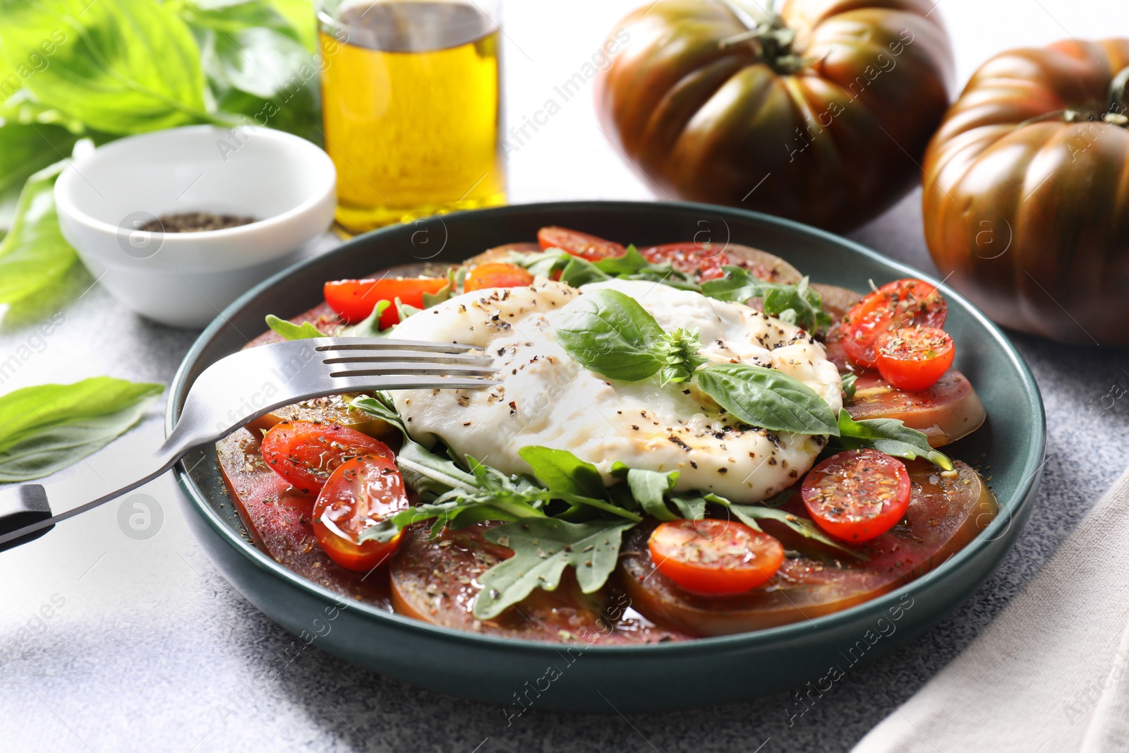 Photo of Delicious fresh burrata salad in bowl served on light gray textured table, closeup