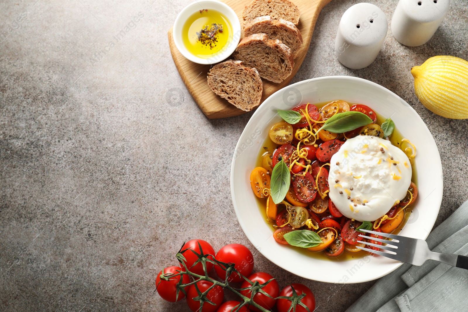 Photo of Delicious fresh burrata salad in bowl served on gray textured table, flat lay. Space for text