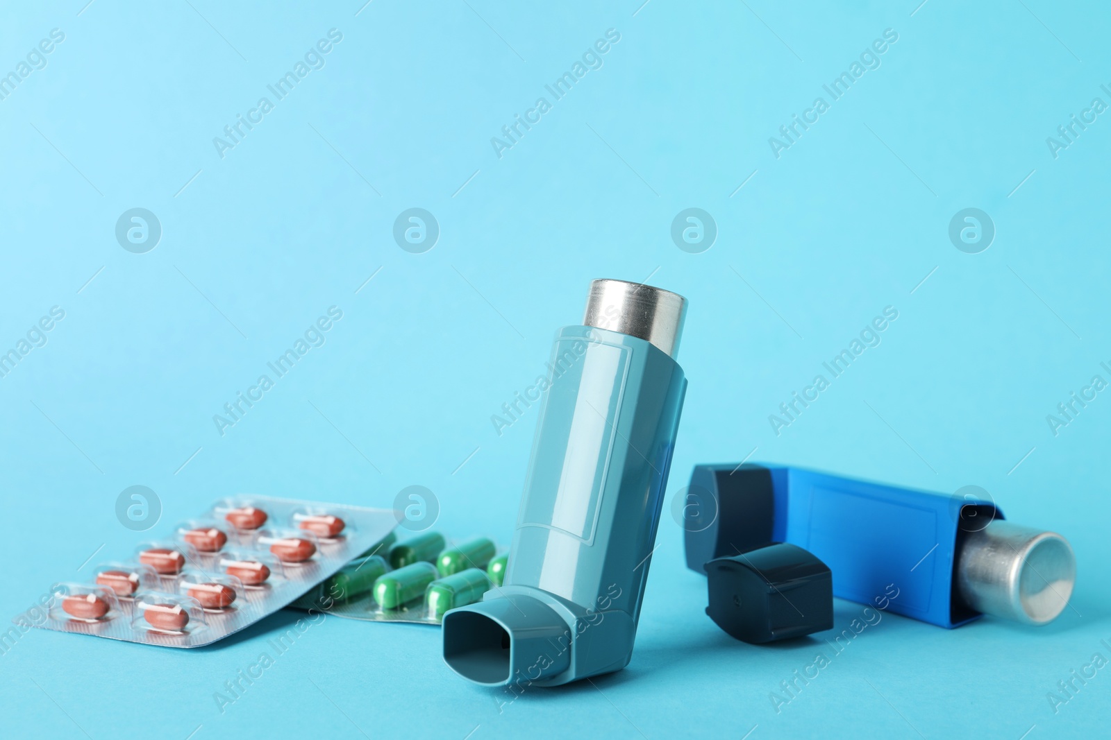 Photo of Inhalers and pills on light blue background, closeup. Asthma treatment