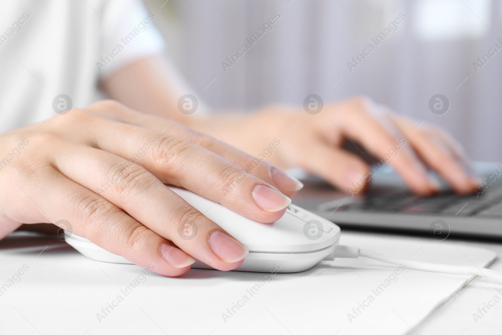 Photo of Woman using computer mouse while working with laptop at white table, closeup