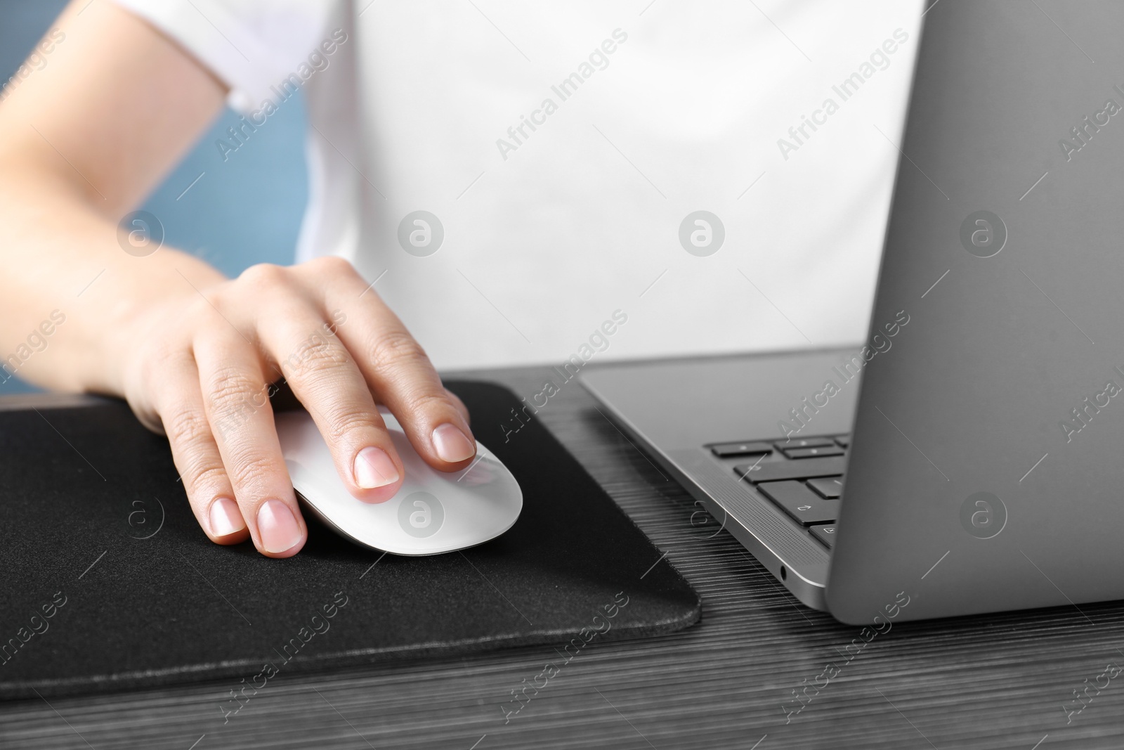 Photo of Woman using computer mouse while working with laptop at black wooden table, closeup