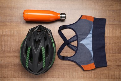 Photo of Bicycle helmet, sportive bra and thermo bottle on wooden background, flat lay