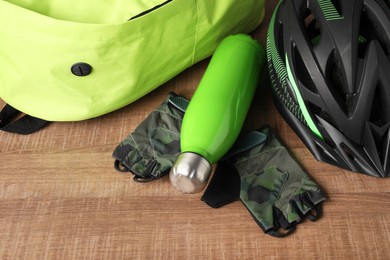 Bicycle helmet, backpack, thermo bottle and fingerless gloves on wooden background, closeup