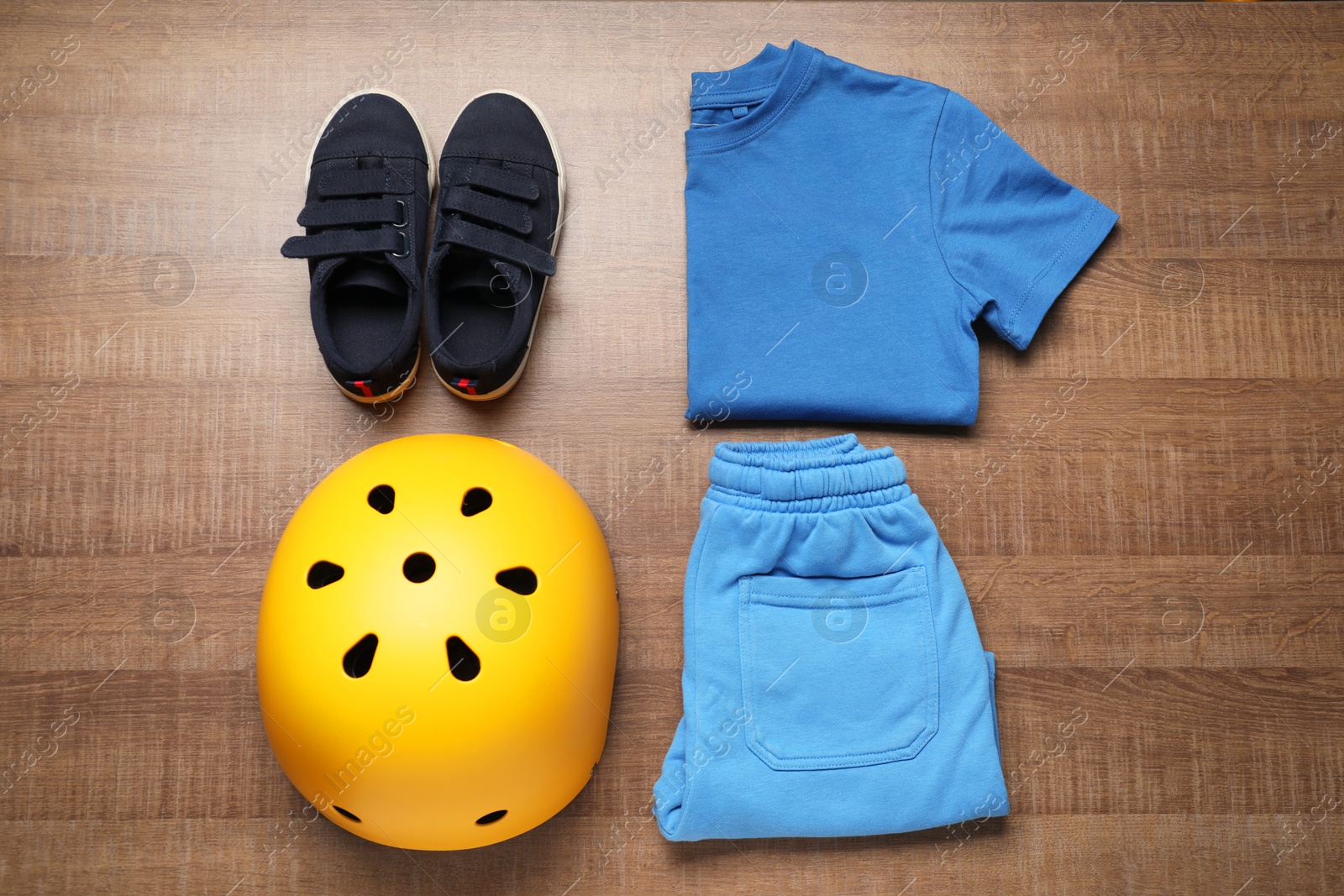 Photo of Bicycle helmet, sneakers and sportswear on wooden background, flat lay