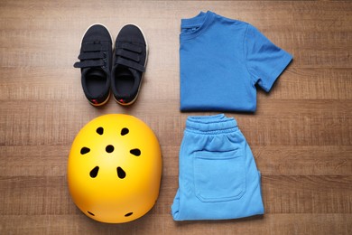 Bicycle helmet, sneakers and sportswear on wooden background, flat lay