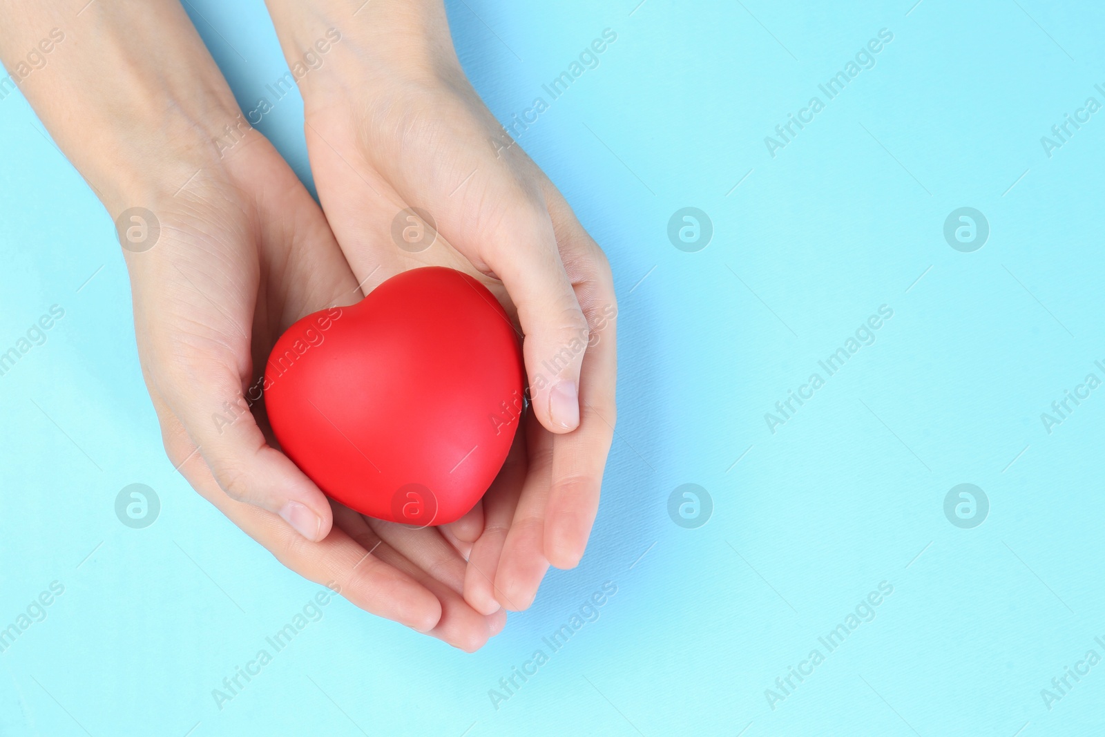 Photo of Woman holding red heart on light blue background, top view. Space for text