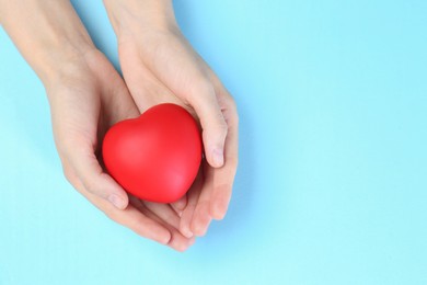 Photo of Woman holding red heart on light blue background, top view. Space for text