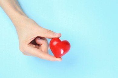 Photo of Woman holding red heart on light blue background, top view