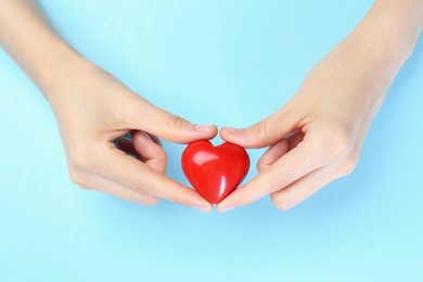 Photo of Woman holding red heart on light blue background, top view