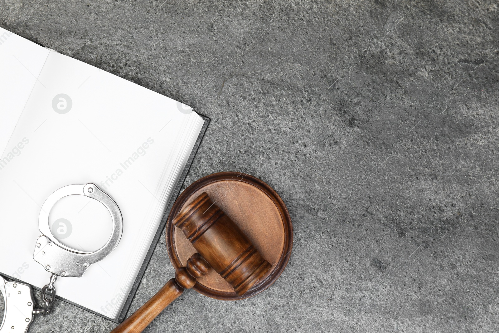 Photo of Book, judge's gavel and handcuffs on gray textured table, flat lay. Space for text