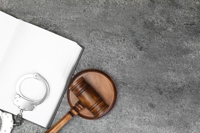 Photo of Book, judge's gavel and handcuffs on gray textured table, flat lay. Space for text