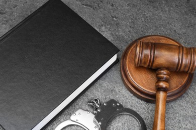 Book, judge's gavel and handcuffs on gray textured table