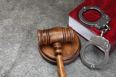 Photo of Book, judge's gavel and handcuffs on gray textured table, space for text