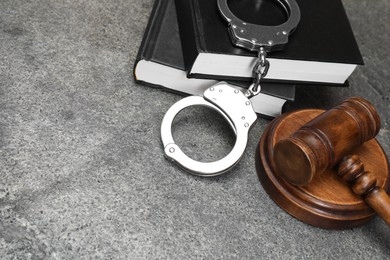 Photo of Books, judge's gavel and handcuffs on gray textured table, space for text