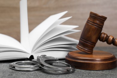 Photo of Book, judge's gavel and handcuffs on gray textured table, closeup