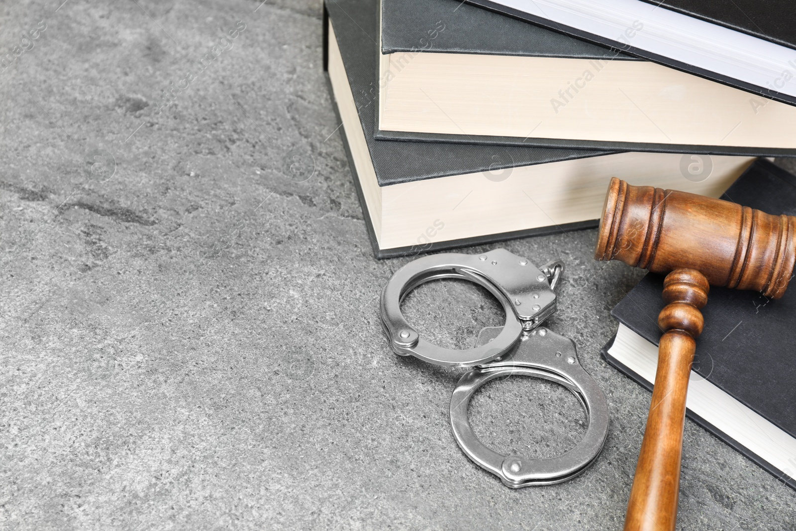 Photo of Books, judge's gavel and handcuffs on gray textured table, space for text