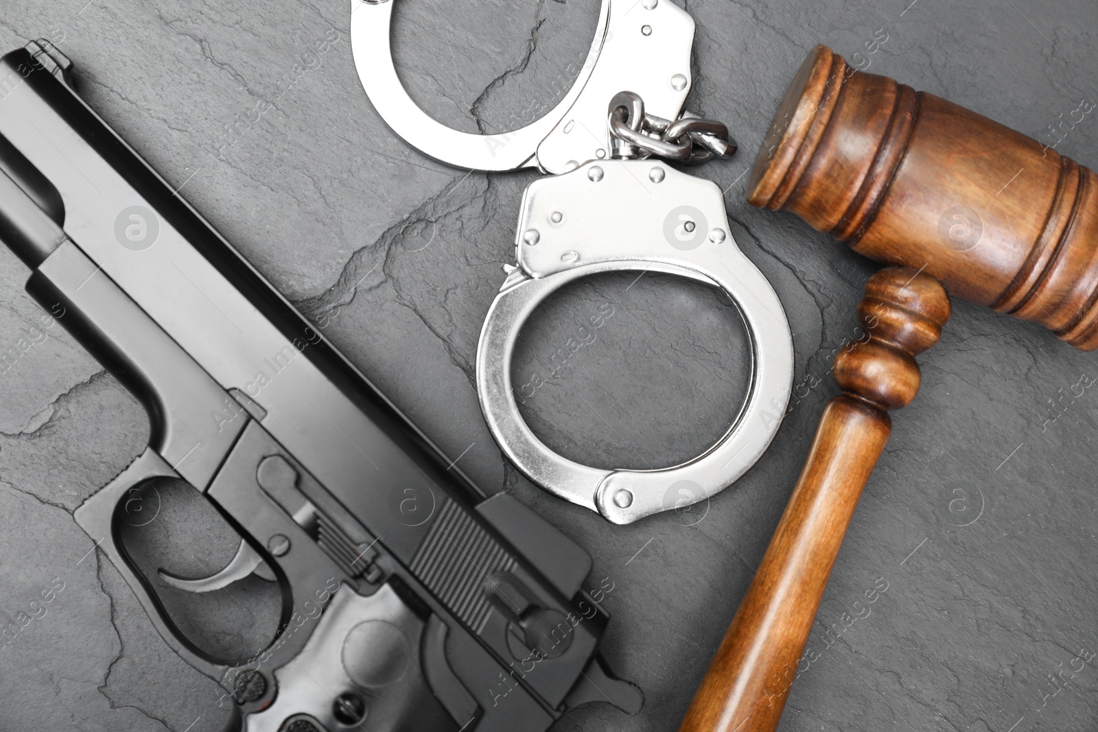 Photo of Judge's gavel, gun and handcuffs on gray textured table, flat lay