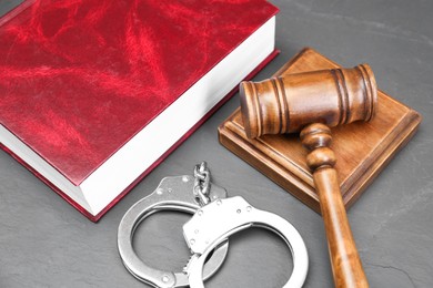 Book, judge's gavel and handcuffs on gray textured table