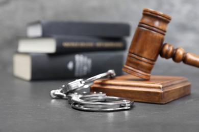 Photo of Books, judge's gavel and handcuffs on gray textured table, selective focus