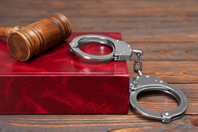 Book, judge's gavel and handcuffs on wooden table, closeup