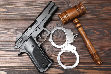 Gun, judge's gavel and handcuffs on wooden table, flat lay