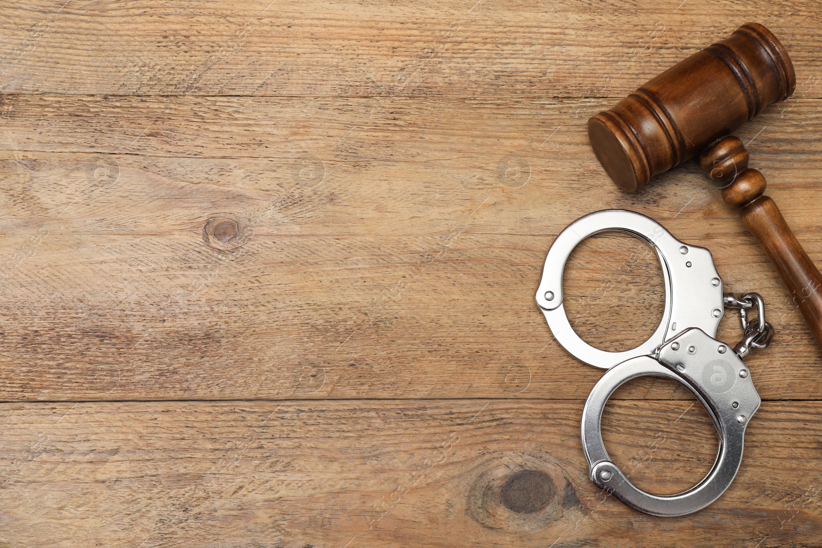 Photo of Judge's gavel and handcuffs on wooden table, flat lay. Space for text