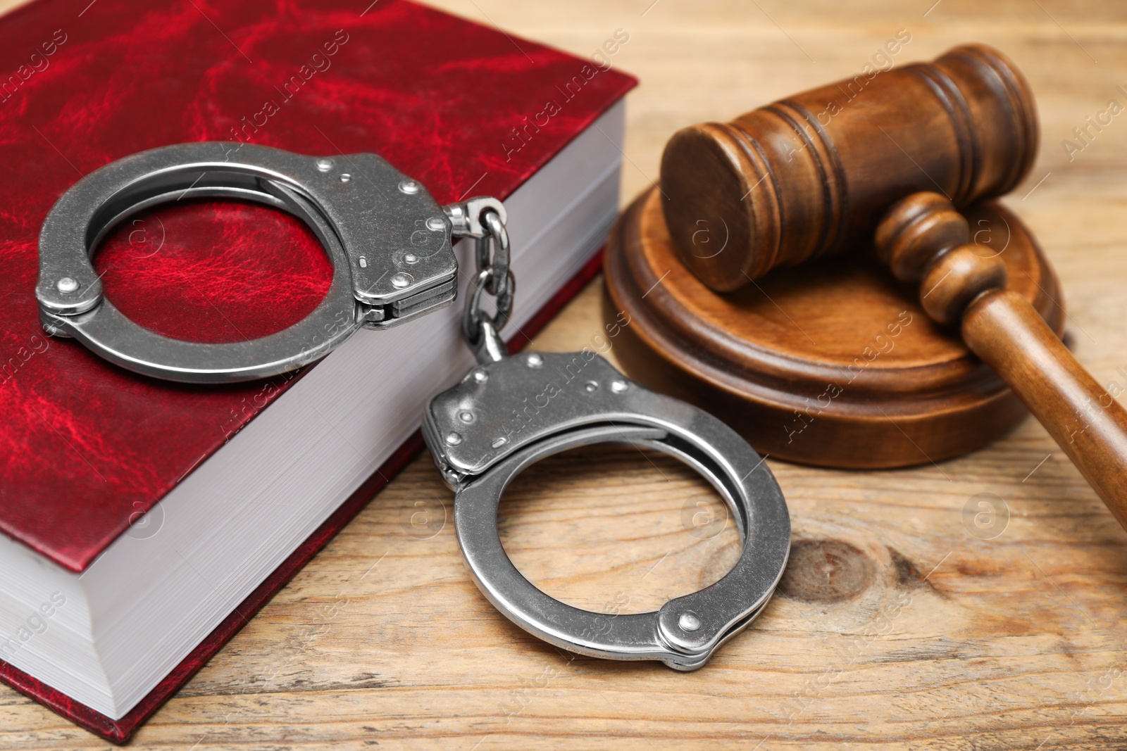 Photo of Book, judge's gavel and handcuffs on wooden table, closeup