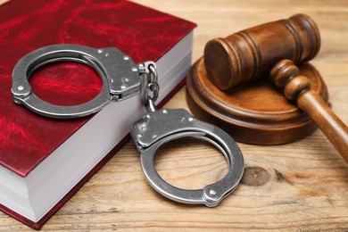 Book, judge's gavel and handcuffs on wooden table, closeup