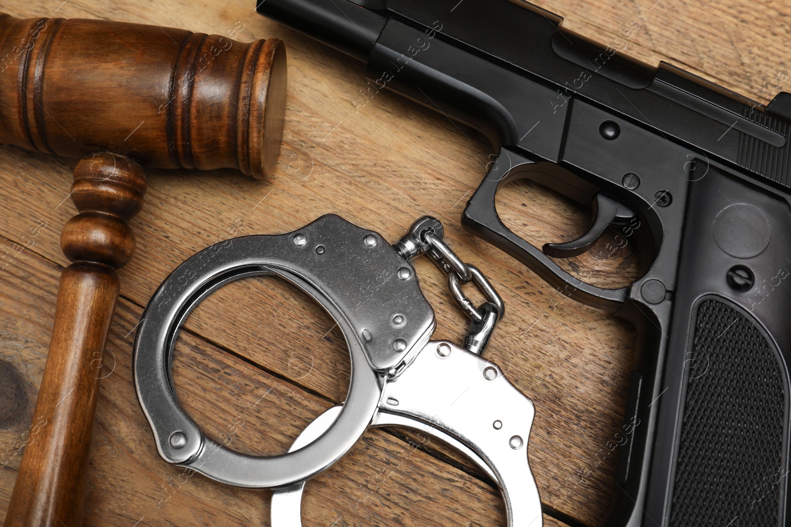 Photo of Gun, judge's gavel and handcuffs on wooden table, flat lay