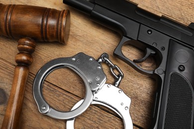 Gun, judge's gavel and handcuffs on wooden table, flat lay