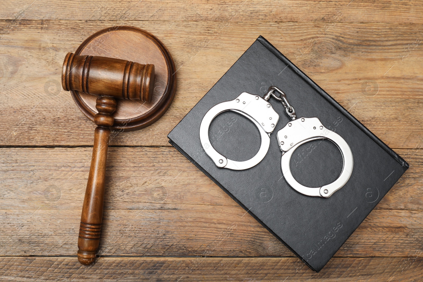 Photo of Book, judge's gavel and handcuffs on wooden table, flat lay