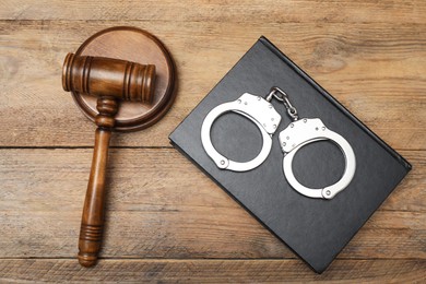 Photo of Book, judge's gavel and handcuffs on wooden table, flat lay