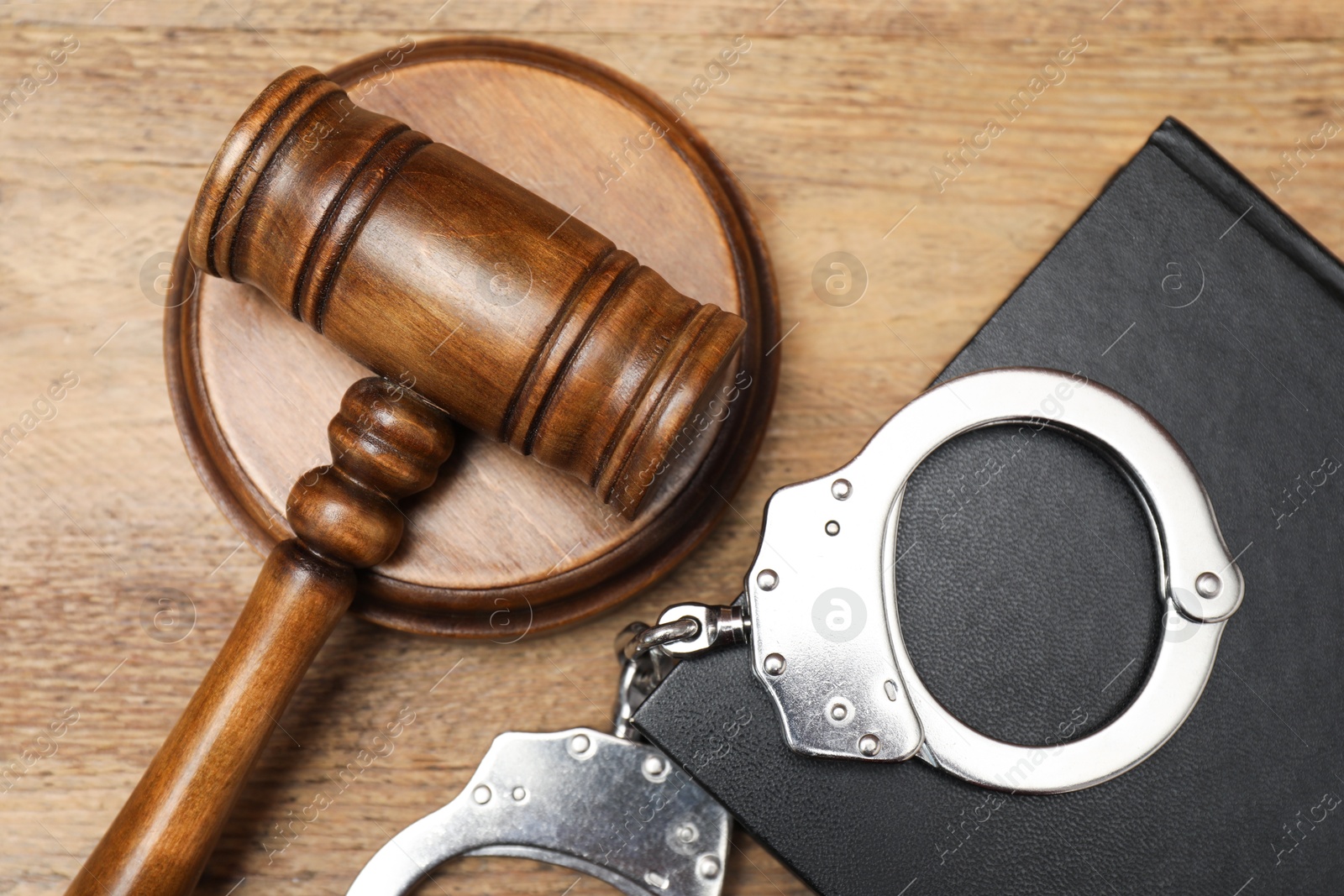 Photo of Book, judge's gavel and handcuffs on wooden table, flat lay