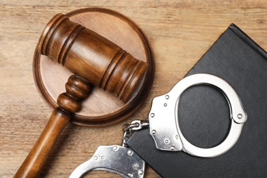 Photo of Book, judge's gavel and handcuffs on wooden table, flat lay