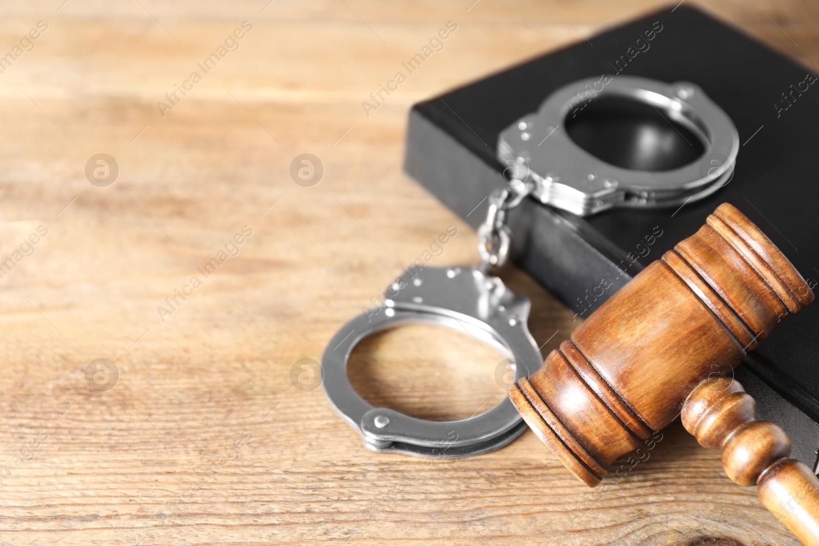 Photo of Book, judge's gavel and handcuffs on wooden table, closeup. Space for text