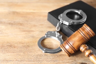 Photo of Book, judge's gavel and handcuffs on wooden table, closeup. Space for text