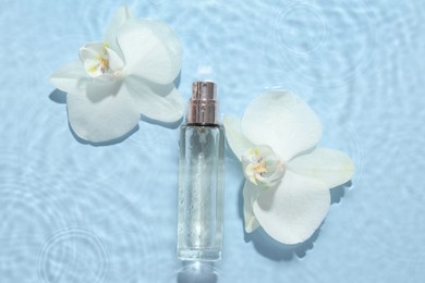 Beautiful orchid flowers and bottle of perfume in water on light blue background, flat lay