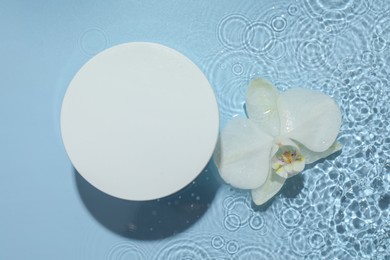 Photo of Beautiful orchid flower and podium in water on light blue background, flat lay. Presentation for product