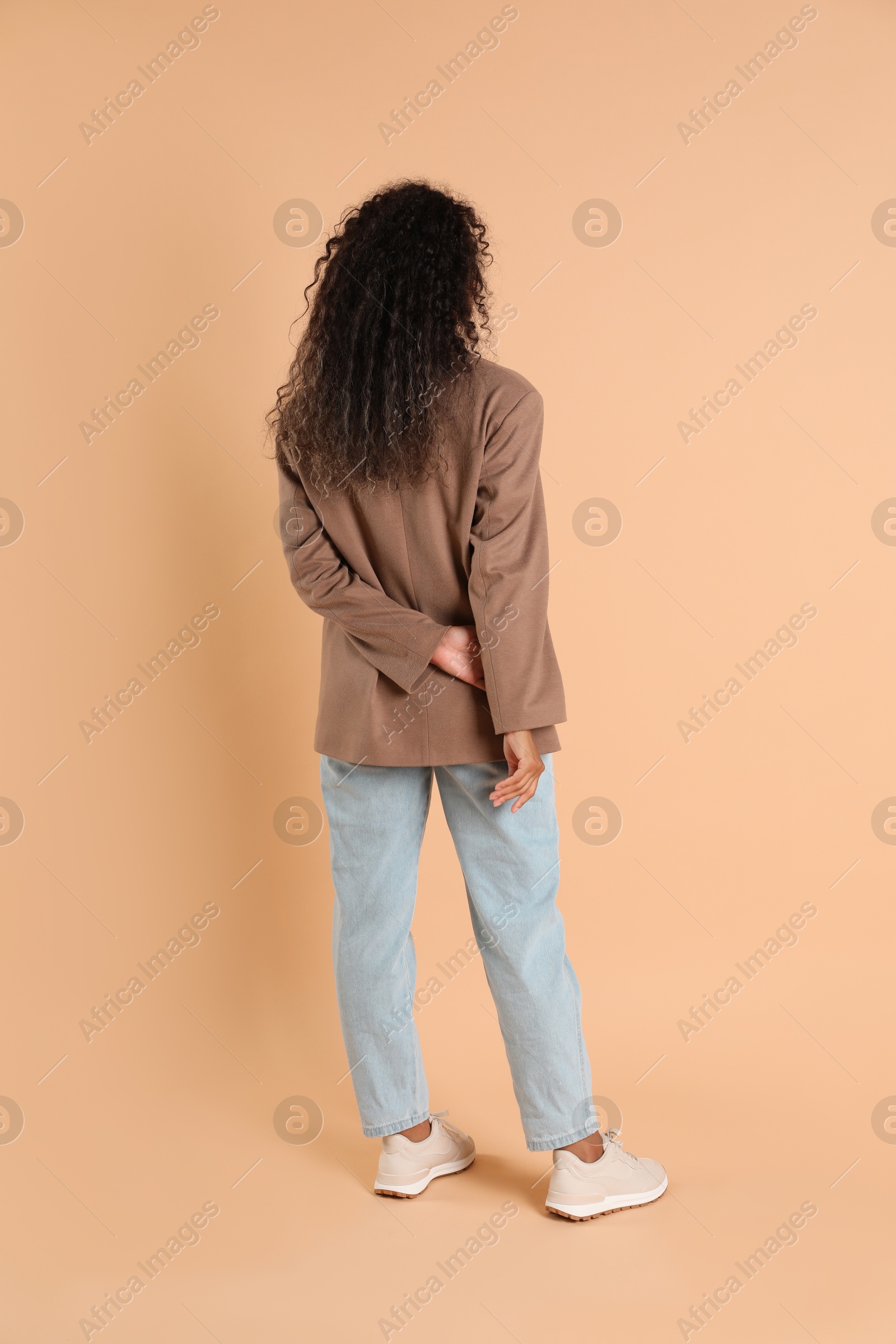 Photo of Woman in stylish jacket on beige background, back view