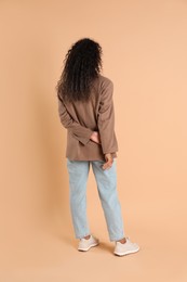 Photo of Woman in stylish jacket on beige background, back view