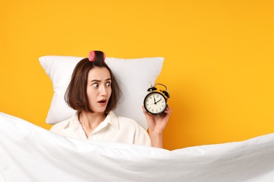 Overslept young woman with alarm clock, pillow and blanket on yellow background. Space for text